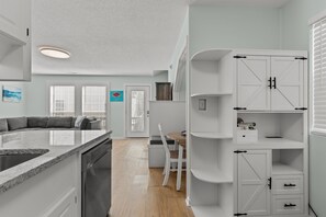 Eine moderne Küche mit integriertem Geschirrspüler, einem Essbereich mit weißem Tisch und Stühlen sowie einem weißen Schrank mit Schubladen und Regalen.