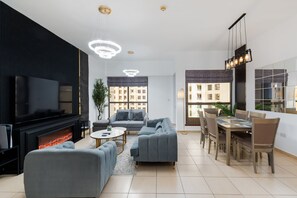 A modern living room with a fireplace, grey sofas, a dining table with chairs, and large windows with city views. - Cozy 3BR Space at JBR, Beach Nearby (Dubai)