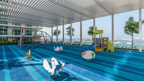 A children's play area with a view of the sea, featuring swings, slides, and a climbing structure. - Stylish Emaar Beachfront 2BR w/ Beach Access (Dubai)
