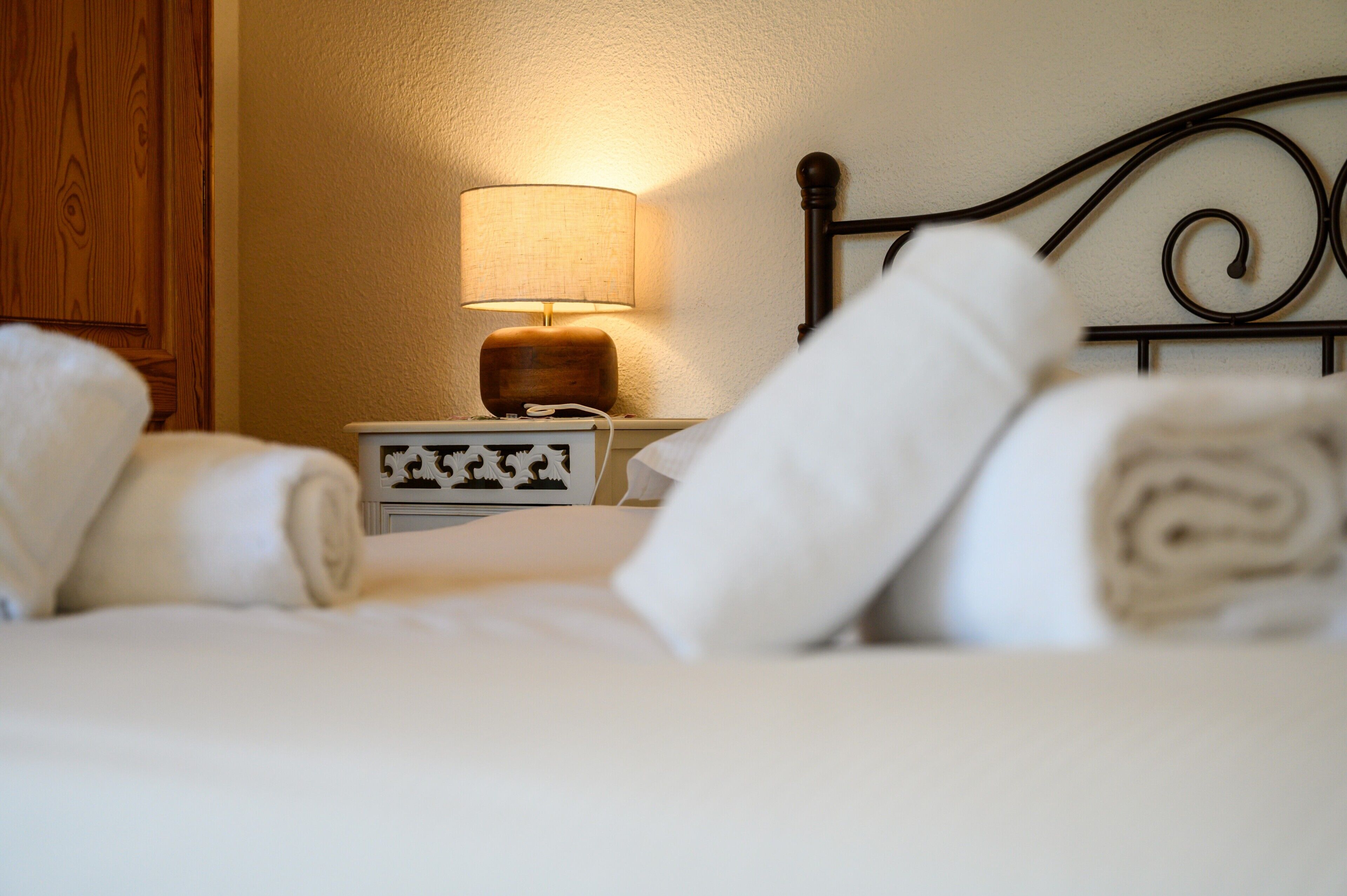 Una cama bien hecha con toallas enrolladas, una lámpara de noche y una mesita con un objeto decorativo.