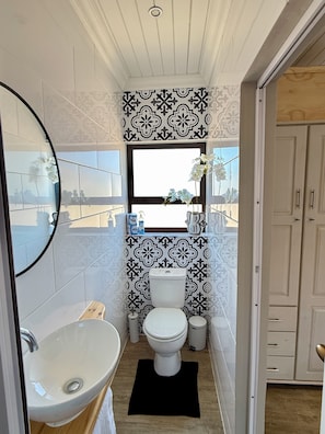 A compact bathroom with a toilet, sink, and window. - Cozy Studio apartment in popular kitesurfing mecca Langebaan with AC (Langebaan)