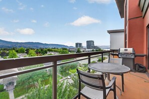 Ein Balkon mit Grill, Stühlen und Blick auf eine Stadtlandschaft und Berge.