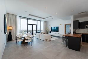 Un espacio habitable moderno con comedor, sofá, televisor, cocina y ventanas amplias.