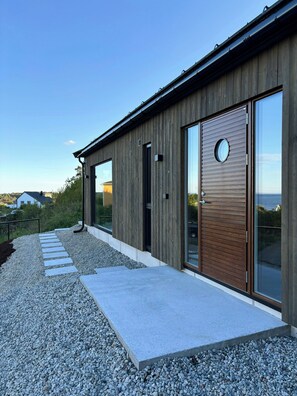 Ein modernes Gebäude mit Holzfassade, großen Glasfenstern und einem Kiesweg, der zum Eingang führt.