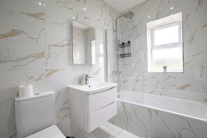 Une salle de bain comprenant des toilettes, un lavabo, un miroir, une douche et une baignoire.