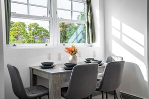 Ein Essbereich mit einem Tisch für vier Personen, einer Blumenvase und Blick auf Bäume durch ein Fenster.