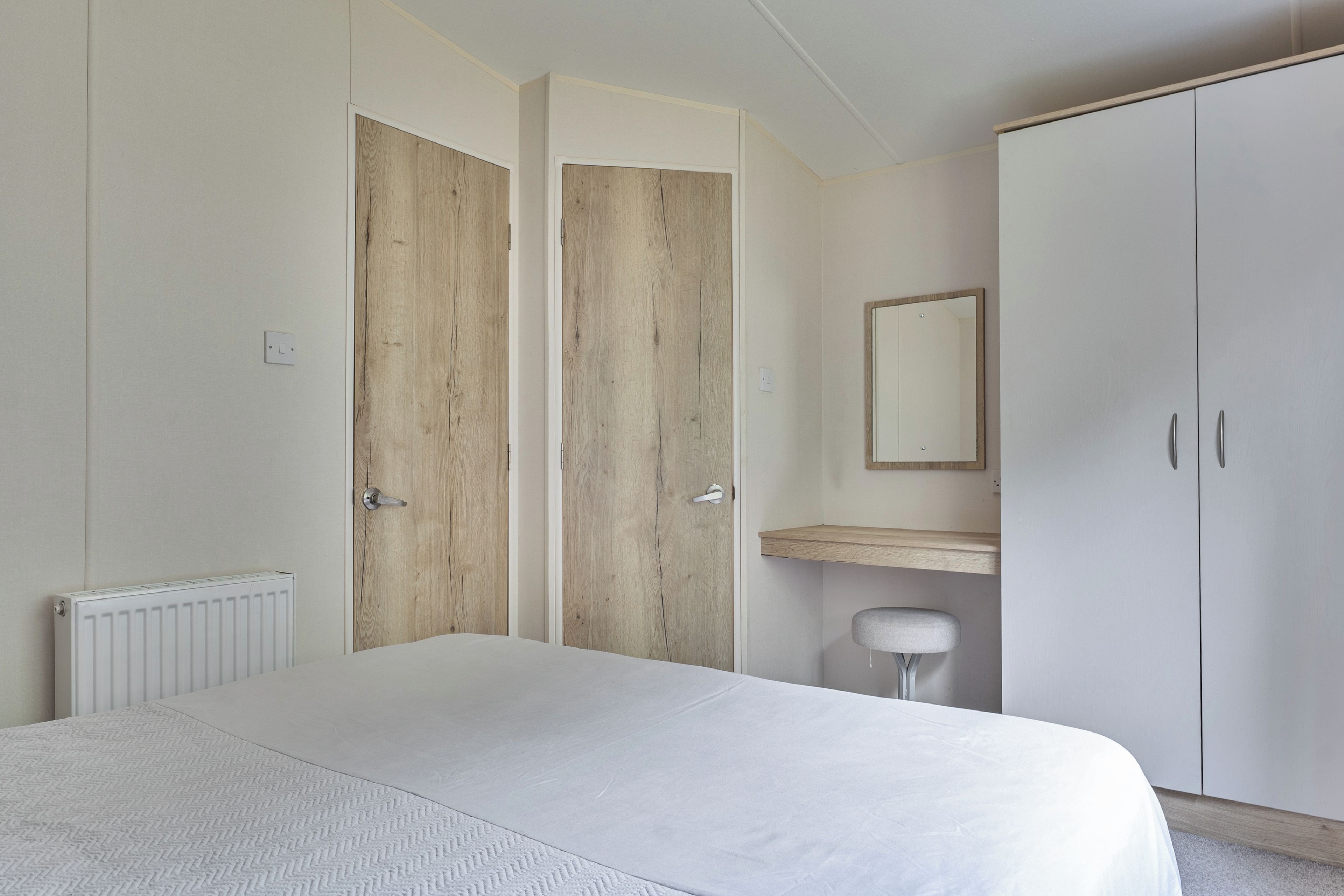 Ein Schlafzimmer mit Bett, Kleiderschrank, Spiegel und Heizkörper.