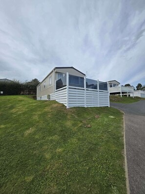 A mobile home with a fenced deck area, a grassy yard, and a paved driveway. - Ty Dee Seaview Escapes (Looe)