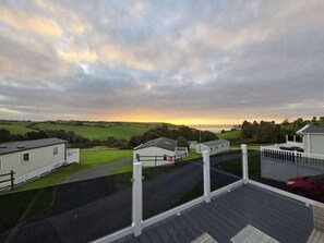A residential area with houses, a paved driveway, and a view of the sunset over a green landscape.