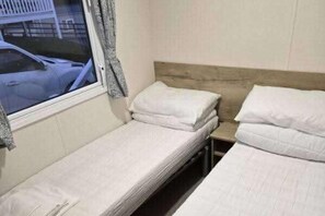 Una cama individual con cabecera de madera, una ventana con vistas a un estacionamiento y una cortina.
