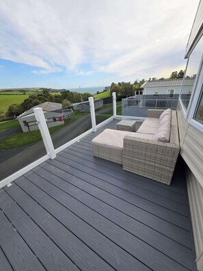 A balcony with a wicker sofa and a view of a road and fields. - Ty Dee Seaview Escapes (Looe)