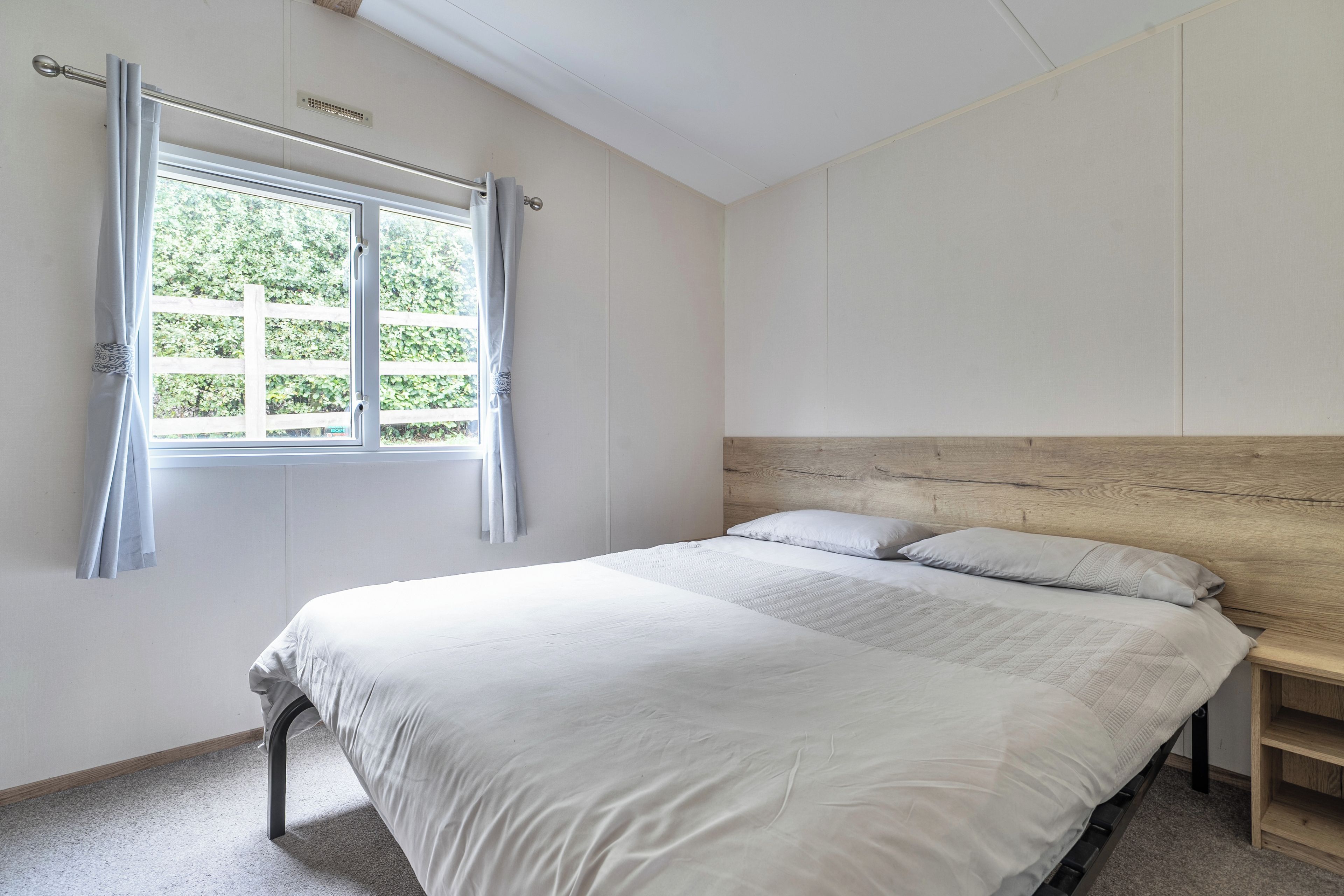 Un dormitorio con cama, ventana con cortinas y cabecero.