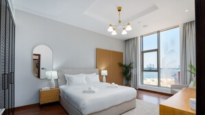 A modern hotel room with a large bed, a desk, a mirror, and a view of the beach. - 2BR at the Palm | Balcony, Pool, Gym & Beach (Dubai)