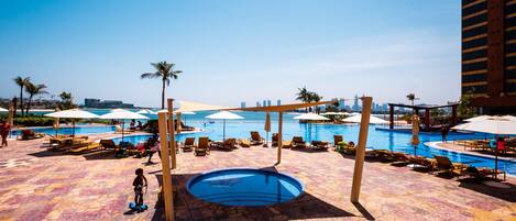 A pool area with multiple pools, lounge chairs, umbrellas, and a tiled floor.