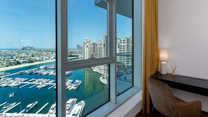 Une chambre située dans un immeuble de grande hauteur, dotée d’une grande fenêtre donnant sur un port de plaisance et sur le paysage urbain.