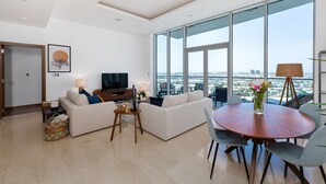 Un salon moderne doté d’une grande fenêtre, d’un téléviseur à écran plat, d’un canapé, d’une table basse et d’une table à manger avec des chaises.