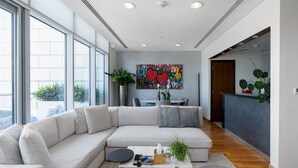 Ein modernes Wohnzimmer mit einem großen, weißen Ecksofa, einem Couchtisch mit Fernbedienungen und einem farbenfrohen abstrakten Gemälde an der Wand.