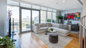 Ein großzügiges Wohnzimmer mit einer großen Eckcouch, einem Couchtisch und Blick auf die Stadt durch raumhohe Fenster.