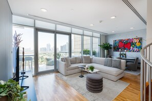 Ein großzügiges Wohnzimmer mit einer großen Eckcouch, einem Couchtisch und Blick auf die Stadt durch raumhohe Fenster.