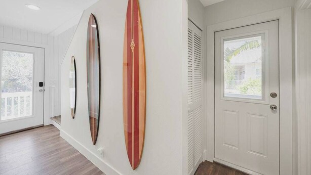 A hallway with two surfboards mounted on the wall, a white door, and a window with blinds. - Sandcastle | Steps to Beach | Pool | Golf Cart (Anna Maria)