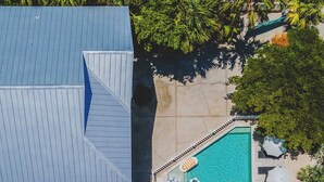 A rooftop pool with a blue roof, surrounded by palm trees and a concrete deck. - Sandcastle | Steps to Beach | Pool | Golf Cart (Anna Maria)