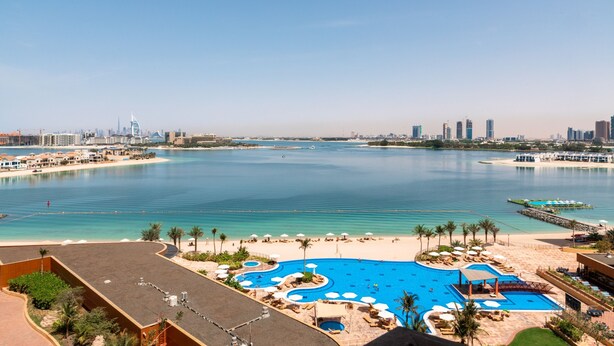 Un resort con una gran piscina, zona de playa y el horizonte de la ciudad al fondo.