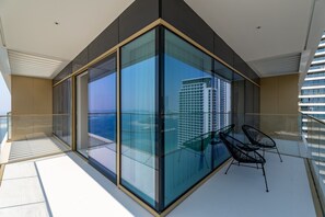 Un balcón moderno con paredes de vidrio, una zona de estar con sillas y vistas a un paisaje urbano.