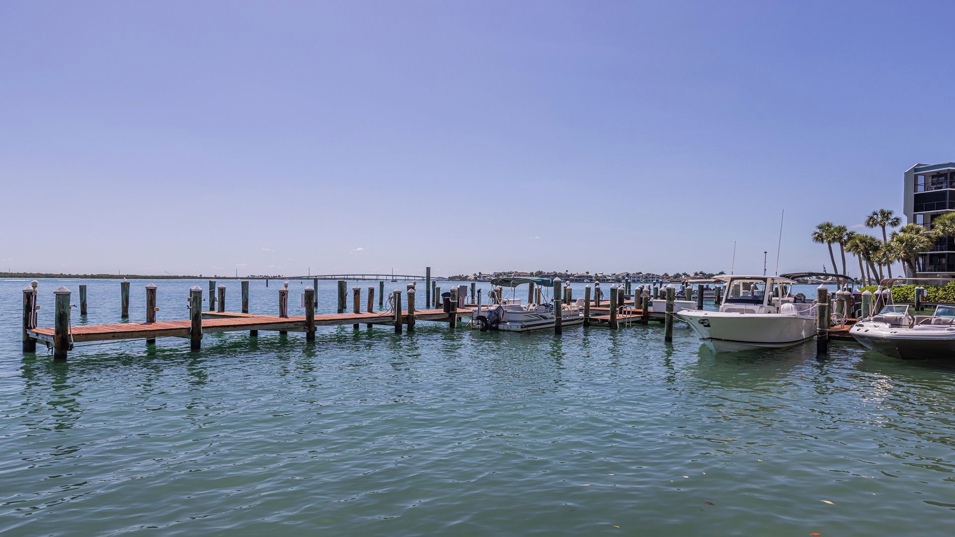 A marina with boats docked, a wooden pier, and a clear blue sky.