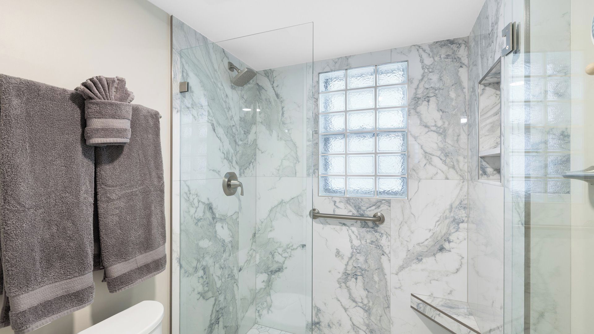 A bathroom with a glass shower enclosure, a marble wall, and a window.