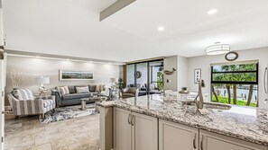 A modern kitchen with granite countertops, a dining area with a white table and chairs, and a living room with a sofa and armchairs. - Come and experience Paradise at its finest at Riverside Club (Marco Island)