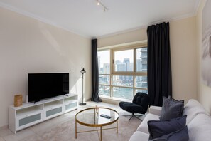 A modern living room with a large window, a flat-screen TV, a round coffee table, a sofa, and a chair. - Chic Dubai Marina 1BR w/ Pool and Gym (Dubai)