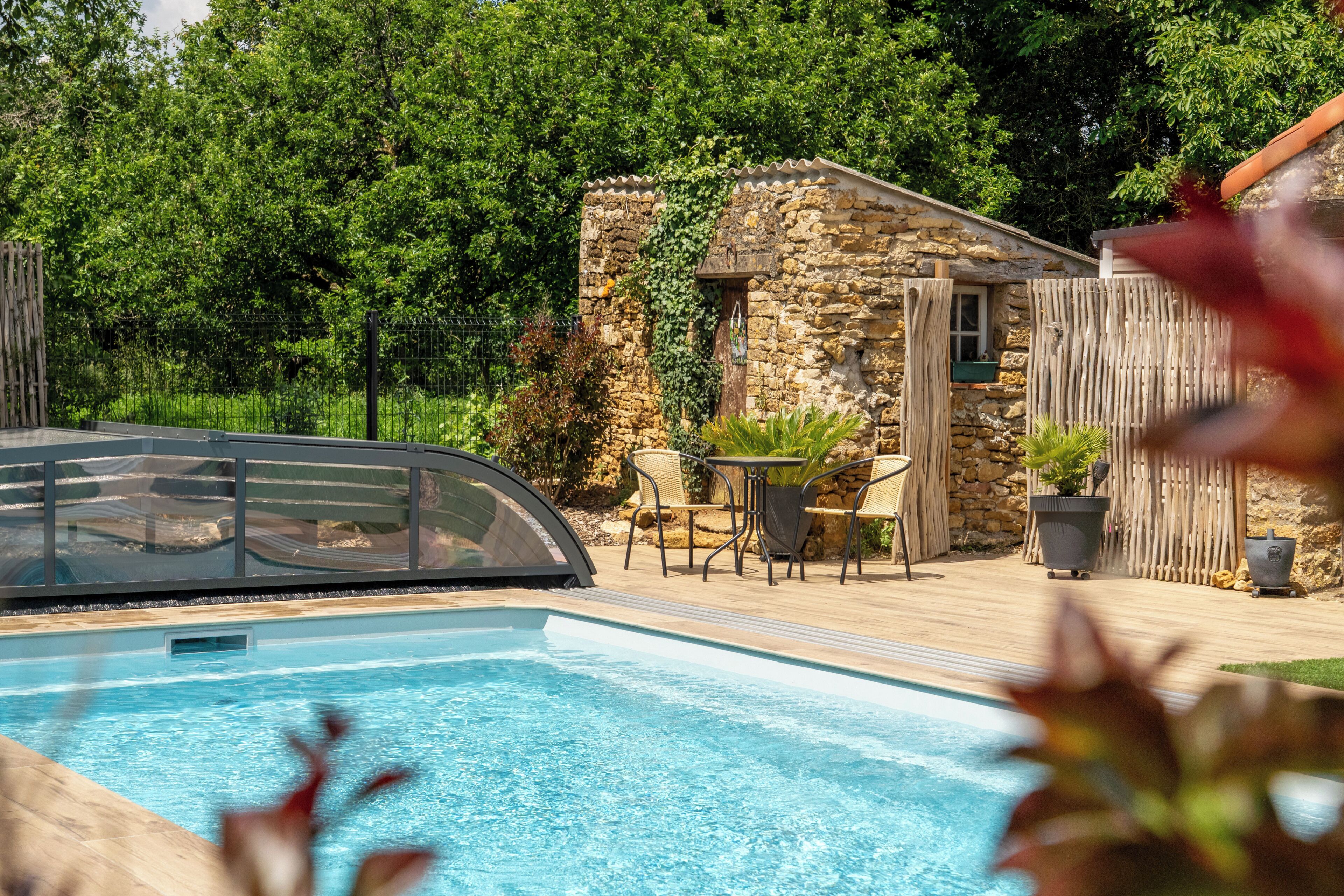 A swimming pool with a covered area, stone walls, and outdoor furniture.