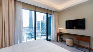 Una camera d'hotel con un letto grande, una scrivania, una sedia, una televisione e vista sulla città attraverso ampie finestre.