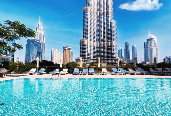 A swimming pool with lounge chairs and a city skyline in the background. - 2BR Address Dubai Opera | Walk to Mall, Burj Khalifa & Opera (Dubai)