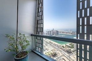 Ein Balkon mit einer Topfpflanze, Blick auf eine Küstenstadt mit Gebäuden und einem Gewässer.