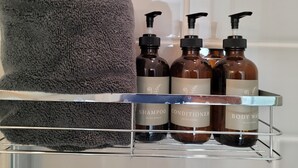 Un estante en el baño con una toalla gris, tres botellas de champú, acondicionador y jabón de cuerpo, y un dispensador.