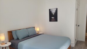 Un dormitorio con una cama, dos mesitas de noche con lámparas, un cuadro en la pared y una puerta.