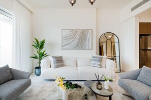 En moderne stue med en hvid sofa, to lænestole, et sofabord, en potteplante og et billede på væggen.