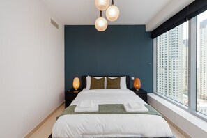 Habitación de hotel con una cama grande, dos lámparas de noche, un ventanal con vistas a la ciudad y una pared de acento azul oscuro.