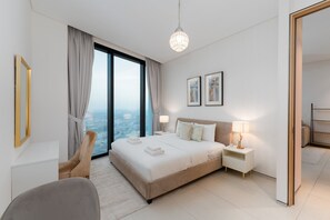 Ein modernes Hotelzimmer mit einem großen Bett, zwei Nachttischen, einem Sessel und Blick auf die Stadt, sowie einem großen Fenster.