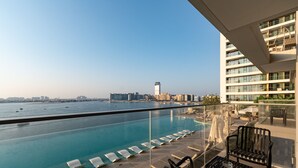 A rooftop pool with lounge chairs, a glass balustrade, and a view of the sea and city skyline. - Chic 2BR w/ Sea Views | Near Marina & JBR (Dubai)