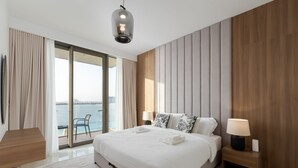 A modern hotel room with a large bed, a nightstand with a lamp, a view of the sea, and a balcony with a chair. - Chic 2BR w/ Sea Views | Near Marina & JBR (Dubai)