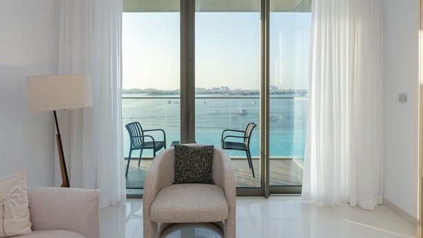 A modern room with a large sliding glass door leading to a balcony with a view of the water and city skyline. - Chic 2BR w/ Sea Views | Near Marina & JBR (Dubai)