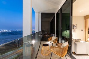 A balcony with a glass railing, wicker furniture, and a city view at dusk. - Urban Studio w/ Balcony Near Downtown and Canal (Dubai)