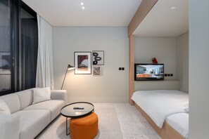 Ein modernes Hotelzimmer mit einer Couch, Hocker, Fernseher und Kunstwerken an der Wand.