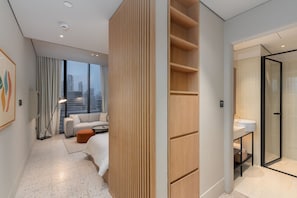 Ein modernes Hotelzimmer mit Blick auf die Stadt, einer Couch, einer Raumteiler aus Holz, einer Glasdusche und einem kleinen Tisch.