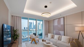 A modern living room with a large TV, a sofa, a coffee table, and a view of a cityscape through large windows. - Exquisite 2BR | Private Beach Access | Near Marina & JBR (Dubai)