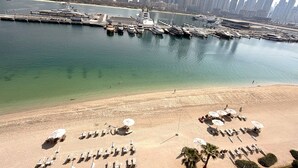 A coastal cityscape with a marina, high-rise buildings, and a sandy beach with sun loungers and umbrellas. - Exquisite 2BR | Private Beach Access | Near Marina & JBR (Dubai)