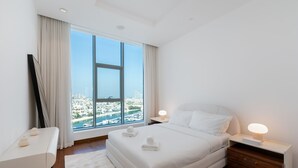 A modern bedroom with a large window, a bed, bedside tables, and a view of a cityscape. - Grand 3BR Beachfront Living | Palm Jumeirah (Dubai)
