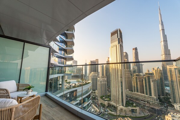 A balcony with wicker furniture, a glass railing, and a cityscape view including the Burj Khalifa. - Prime 2BR Downtown | Iconic Burj View (Dubai)